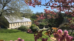 A stone house with a balcony, surrounded by a well-maintained lawn and flowering trees. - B&B Le Clos Saint-Jean - Omaha Beach (Aure sur Mer)