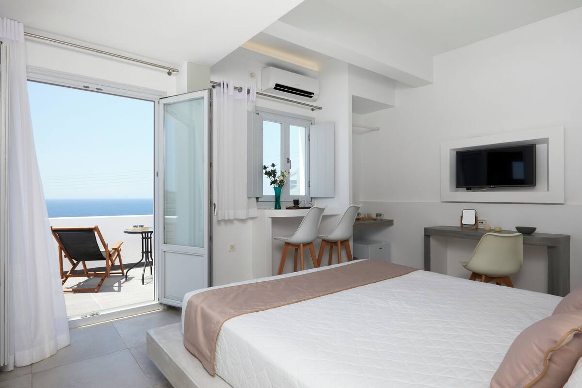 Habitació d'hotel amb llit, escriptori, cadira, televisió i vista al mar.