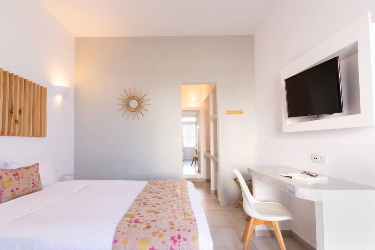 Habitació d'hotel amb llit, escriptori, televisió i una decoració mural amb motius de sol.