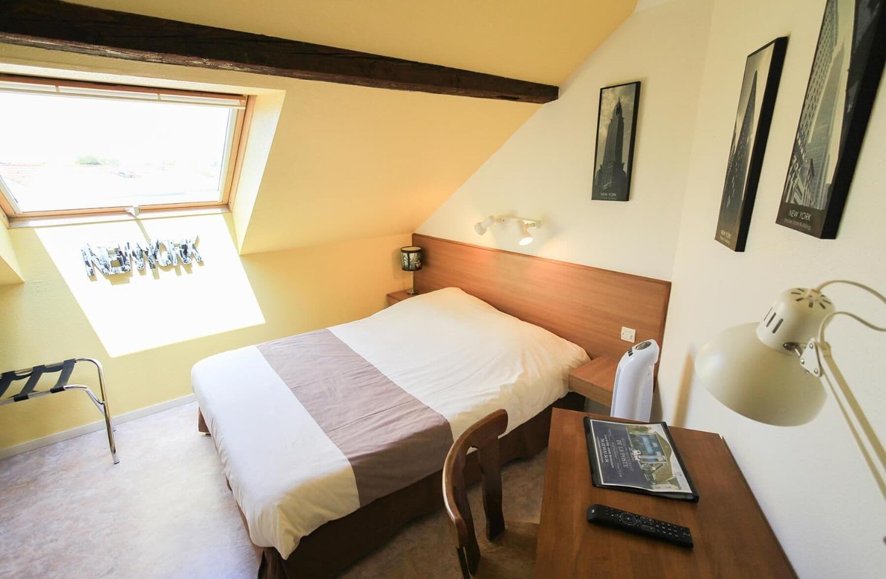 Une chambre à coucher comprenant un lit, un bureau, une chaise, une lampe et une fenêtre donnant sur l’extérieur.