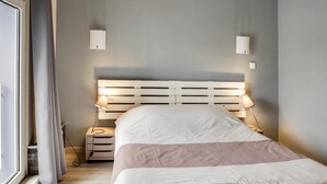 A bedroom with a bed, bedside lamps, a nightstand, and a window with curtains. - Hotel Restaurant De La Poste (Bantzenheim)