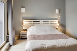 Un dormitorio con cama, lámparas de noche, mesita de noche y ventana con cortinas.