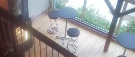 Una habitación con una escalera de madera, un televisor y tres mesas redondas.