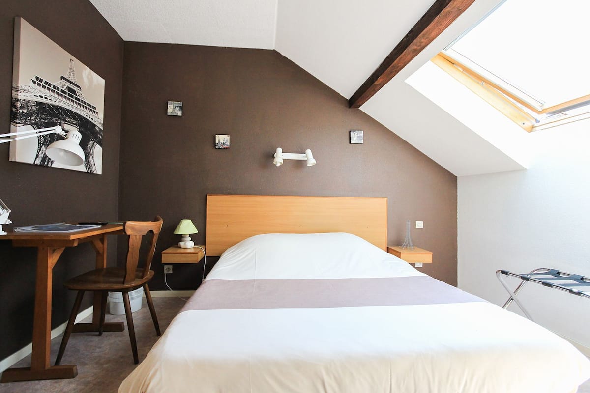 Un dormitorio con cama, escritorio, silla, lámpara y tragaluz.