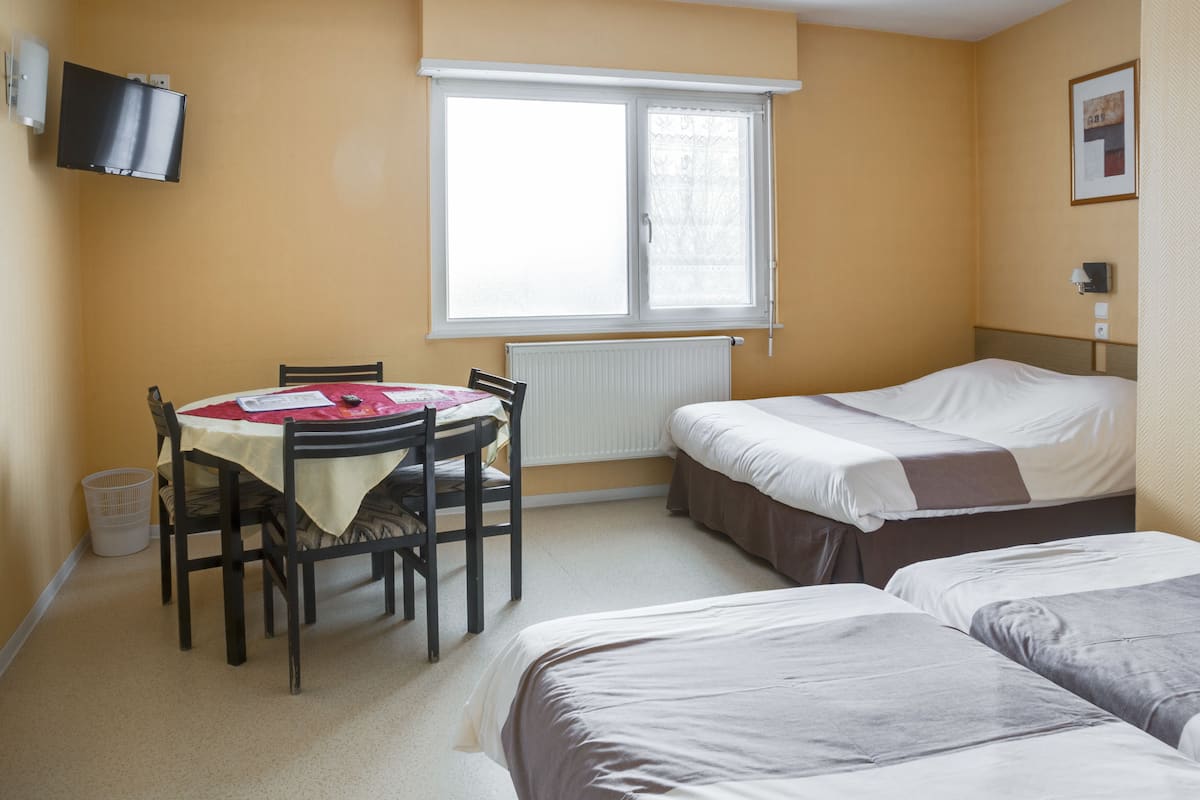 Una habitación con cama, una mesa con sillas, un ventanal y un televisor en la pared.