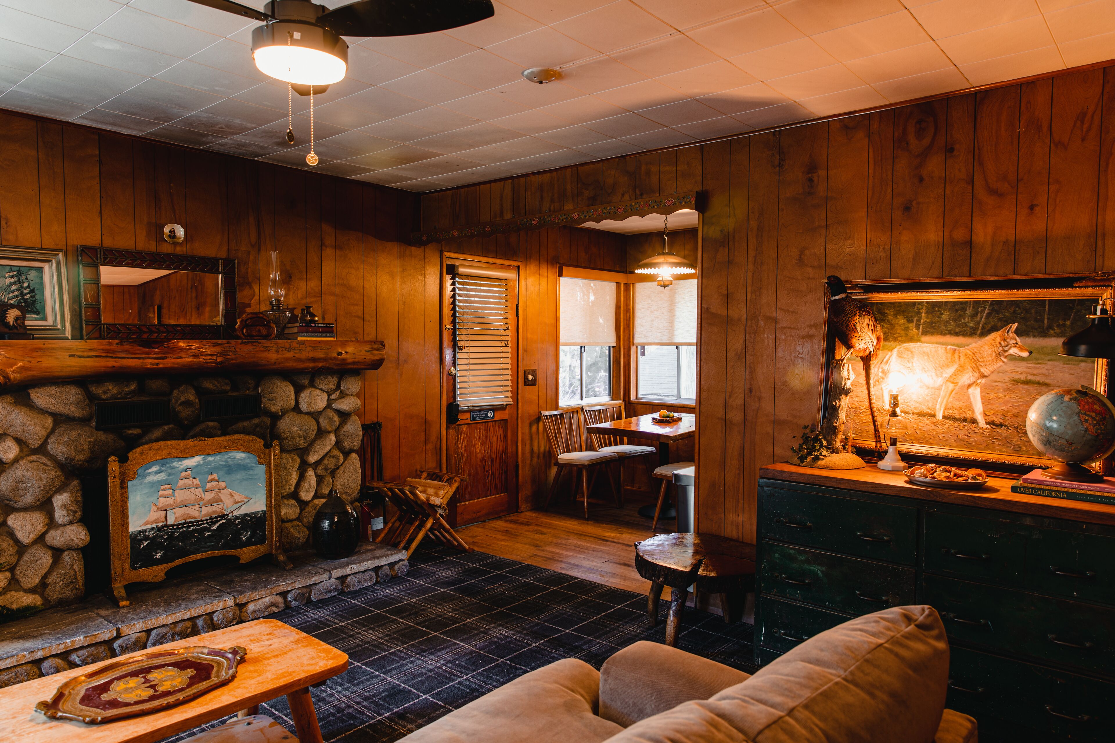 A cozy cabin interior with a stone fireplace, wooden walls, a dining area, and a comfortable seating space.