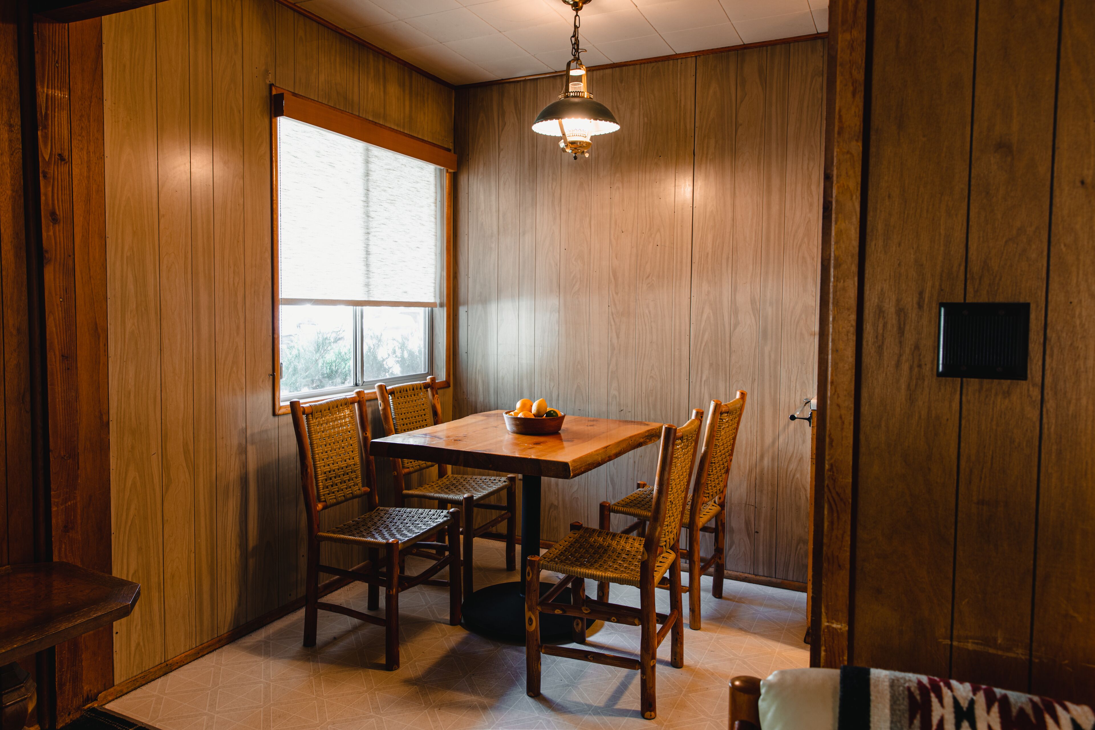 Un coin repas avec une table et des chaises en bois, une fenêtre et un luminaire suspendu.