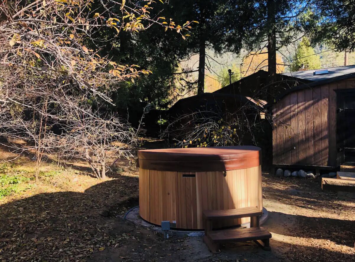 A wooden hot tub with a bench in a wooded area.