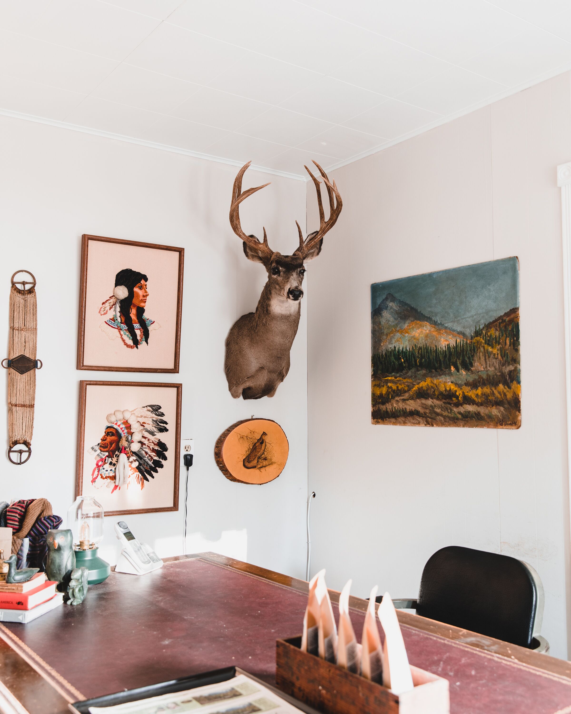 A room with a mounted deer head, framed artwork, and a painting on the wall.