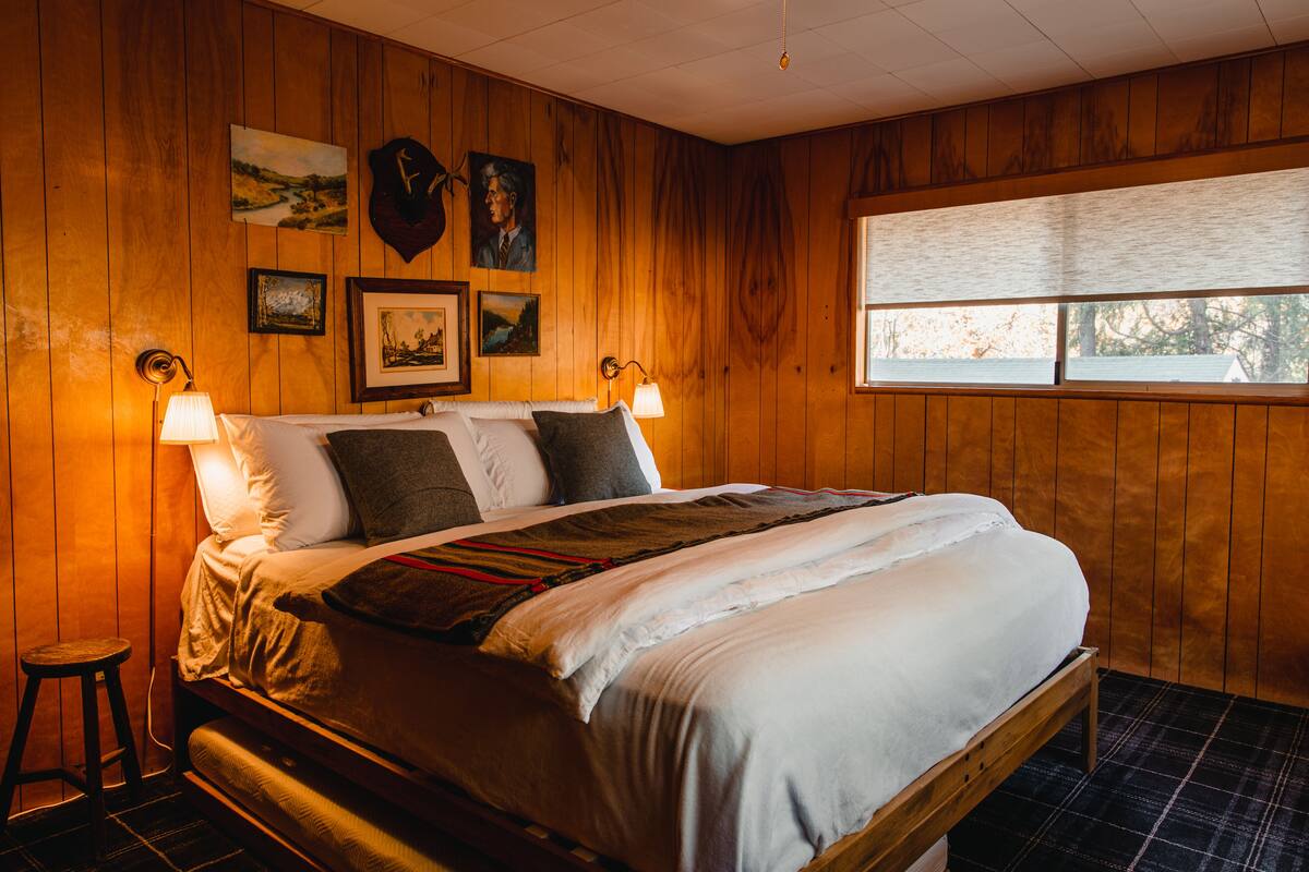 A wooden-paneled bedroom with a bed, two wall-mounted lamps, and framed pictures.