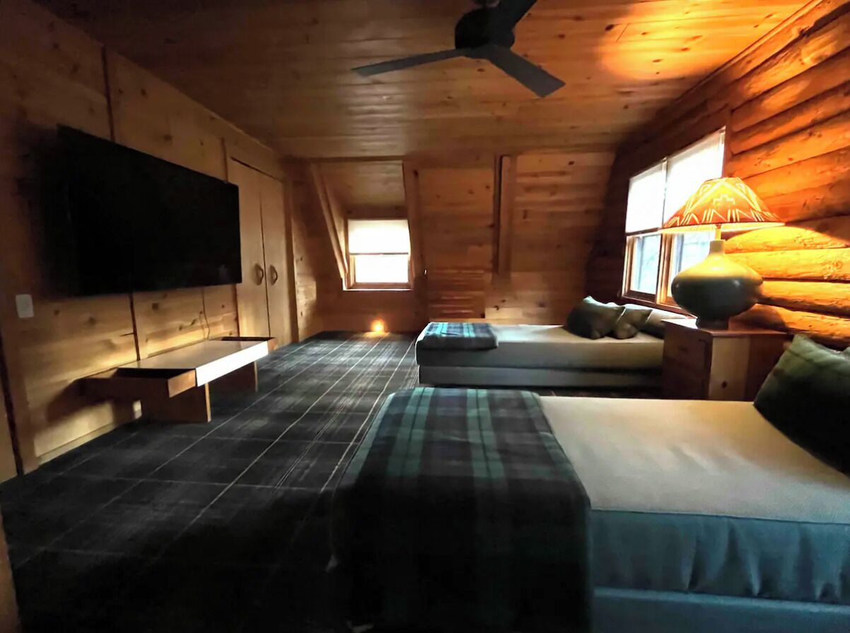 A cabin with a bed, a bench, a TV, and a window.