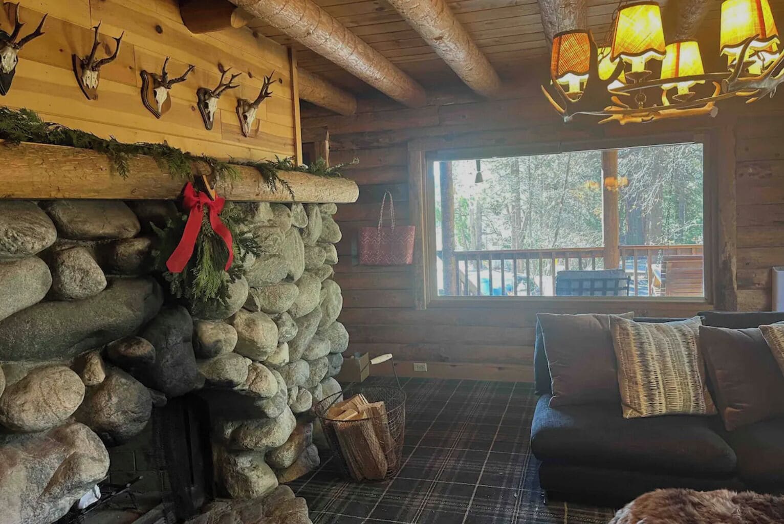 A cozy cabin interior with a stone fireplace, wooden walls, and a view of the outdoors.