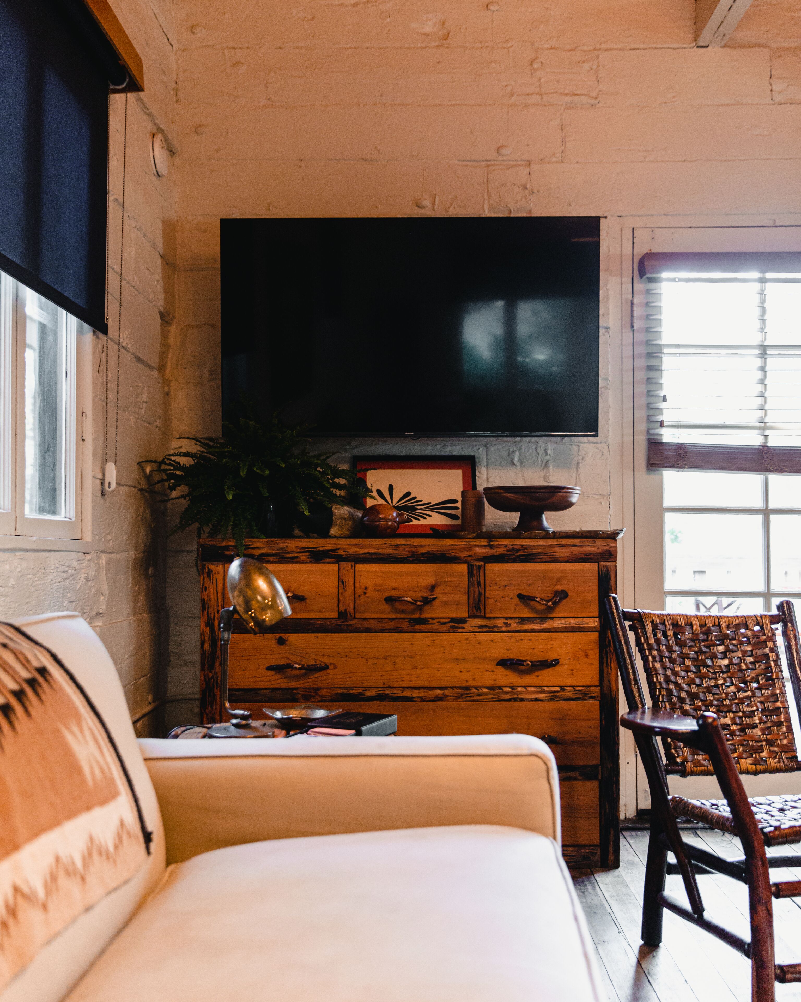 A living room with a wooden cabinet, a television mounted on the wall, a wicker chair, and a sofa.