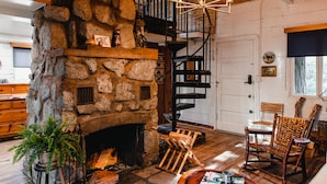 A rustic interior with a stone fireplace, wooden flooring, a spiral staircase, and a dining area with a table and chairs. - The Fireside Inn (Idyllwild)