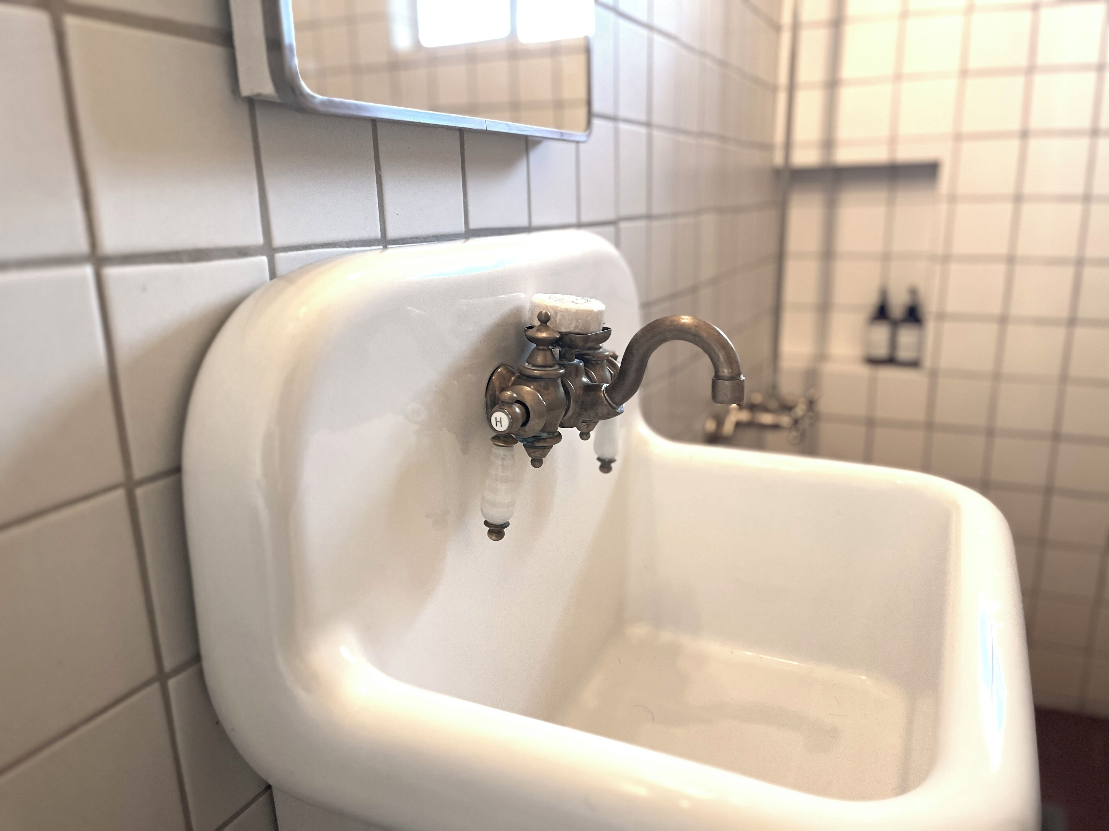 A white ceramic sink with a single-handle faucet, mounted on a tiled wall.