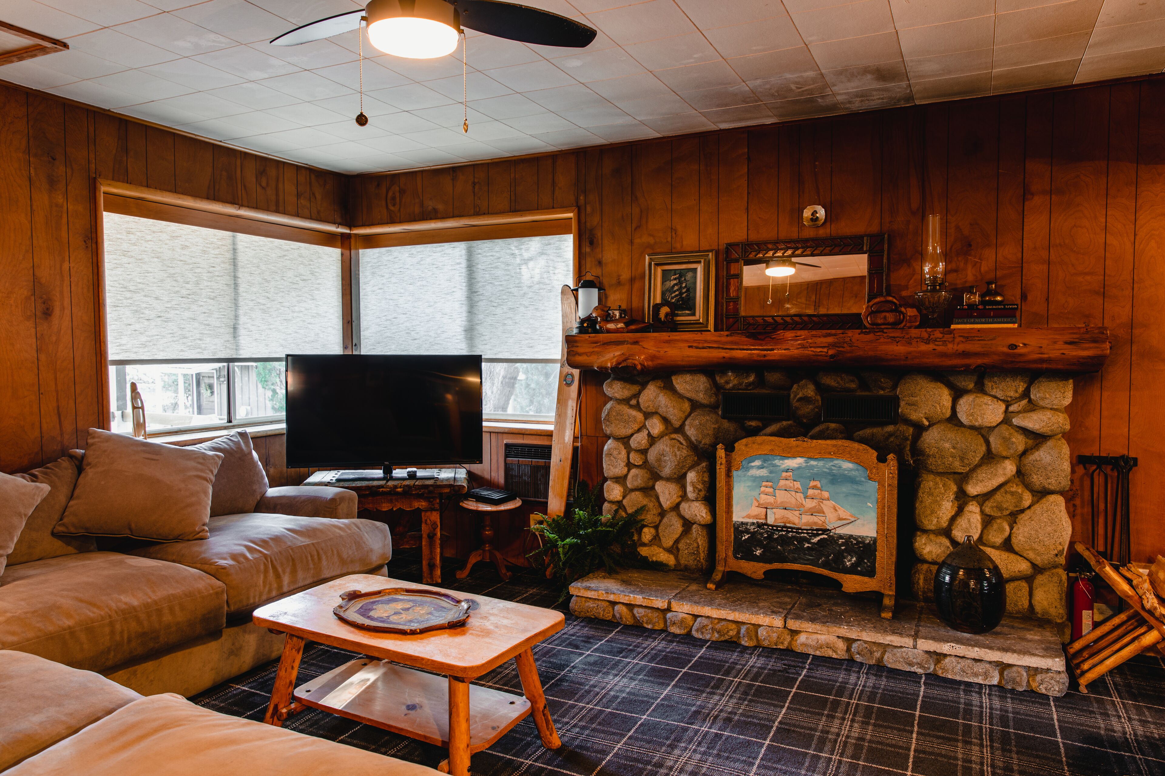 A cozy living room with a stone fireplace, a television, a sofa, and a plaid floor.