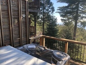 A hot tub on a wooden deck with a railing, surrounded by trees.