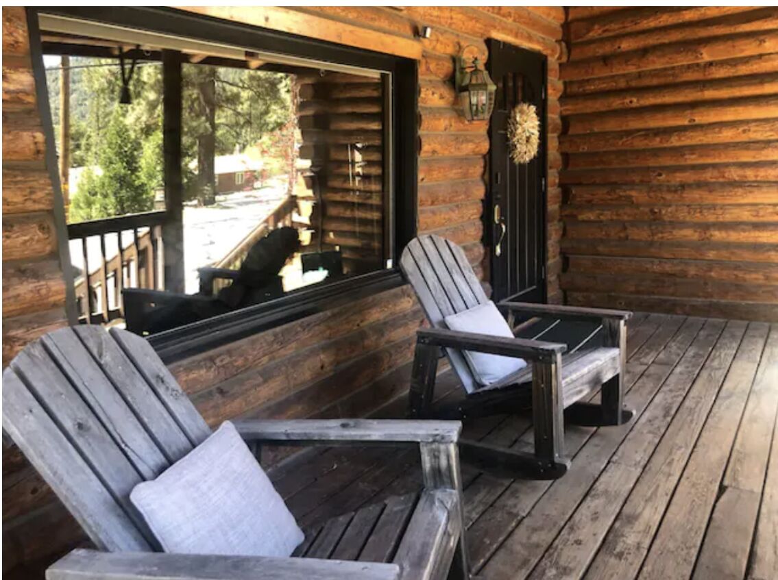 Una cabaña de madera con dos sillas Adirondack en un porche.