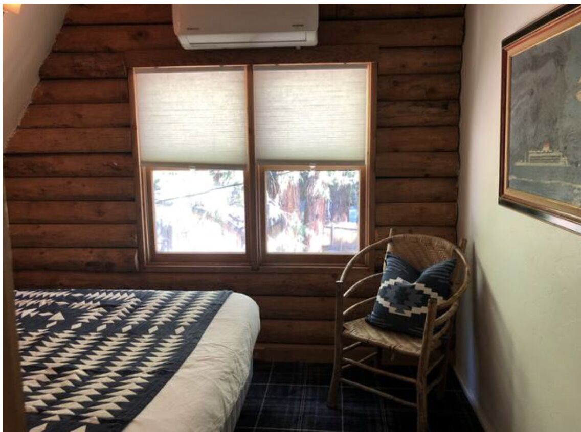 Quarto de cabana de madeira com uma cama, uma cadeira de balanço e uma janela com persianas.