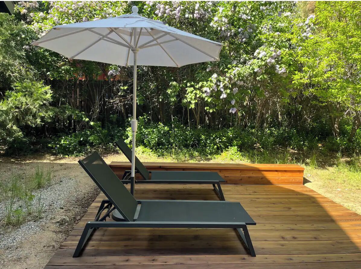 A wooden deck with two lounge chairs and a white umbrella.