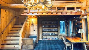 A log cabin interior with a staircase, bookshelves, a chandelier, and a dining area. - The Fireside Inn (Idyllwild)