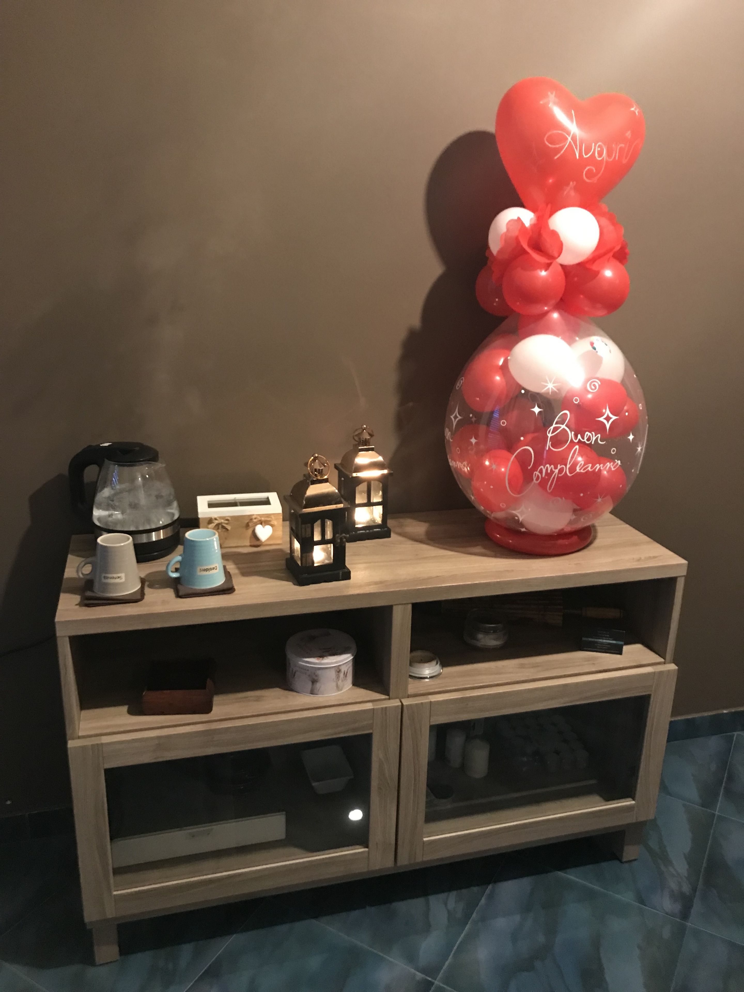 Een houten console tafel met een koffiezetapparaat, twee kopjes, een lantaarn en een decoratieve ballonopstelling.