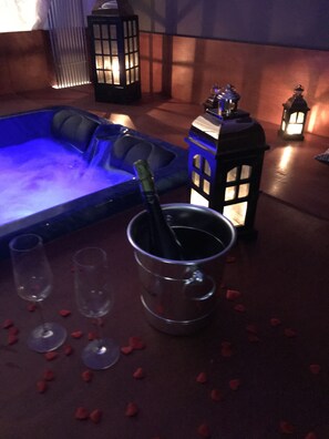 A room with a blue-lit seating area, a metal bucket with a bottle, and two empty glasses on a table with scattered rose petals. - Dimora nel Benessere (Monopoli)