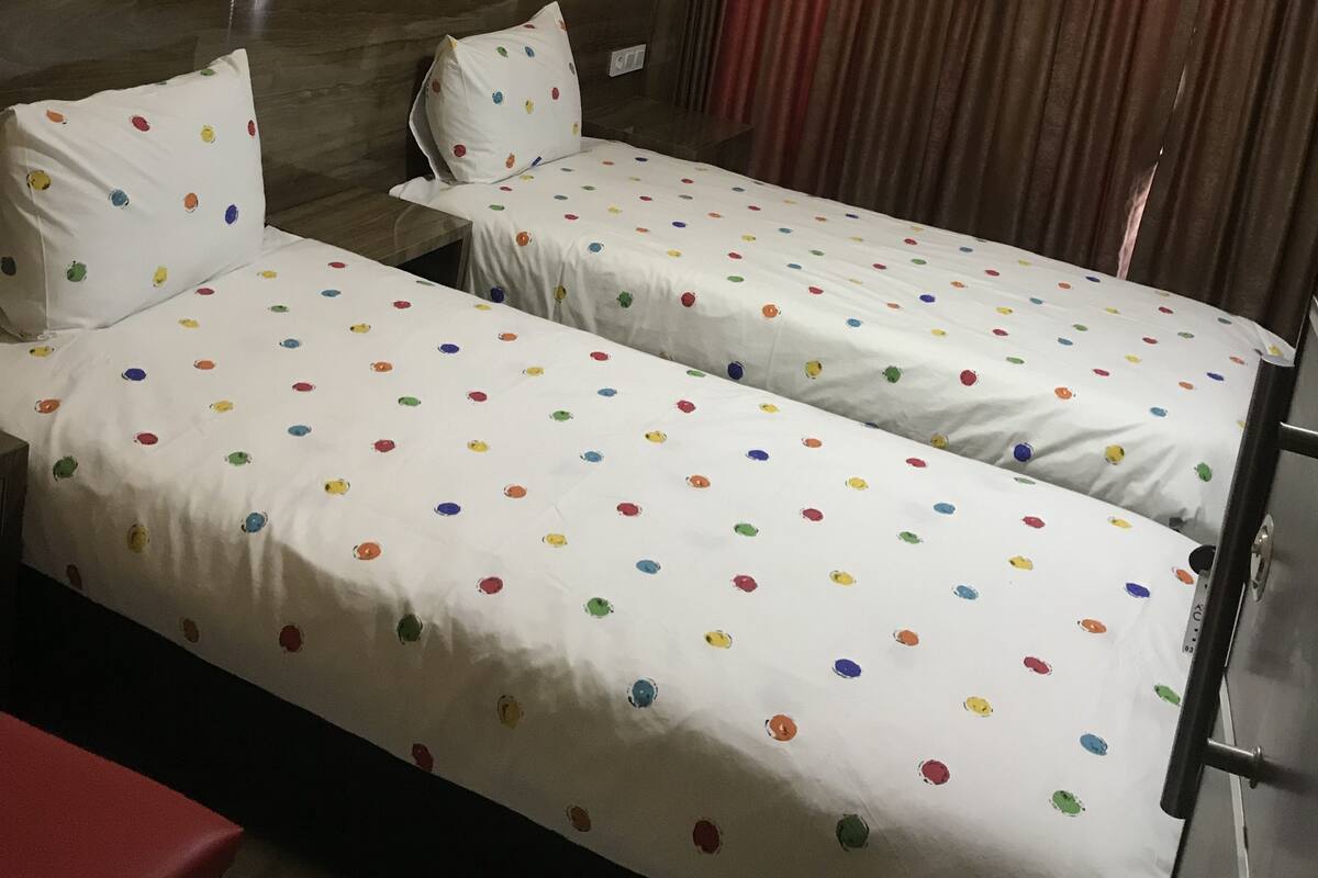 A hotel room with two single beds, a red table, and a curtain.