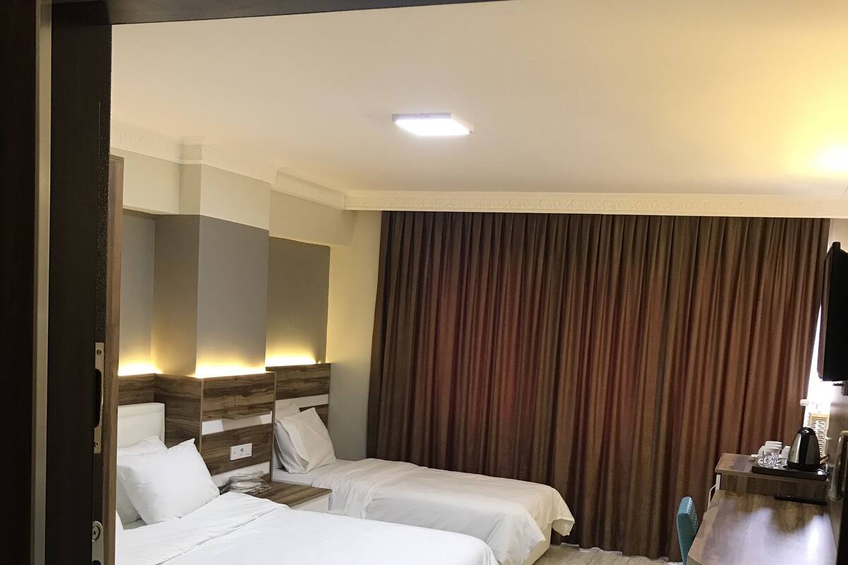 A hotel room with two beds, a desk, a chair, a TV, and a curtain.