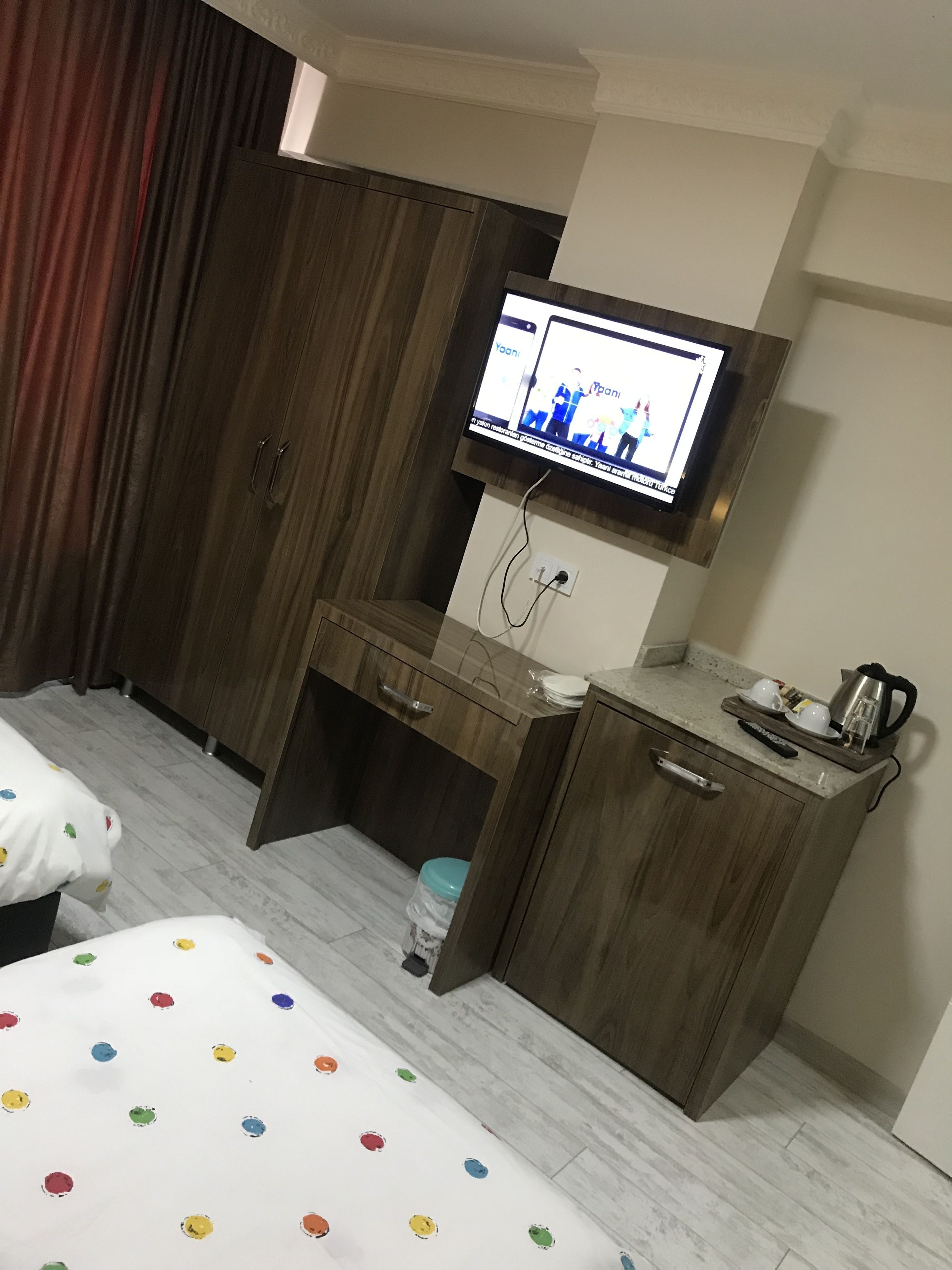 Habitación de hotel con cama, escritorio, televisor montado en la pared y un pequeño armario.