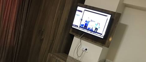 Habitación de hotel con cama, escritorio, televisor montado en la pared y un pequeño armario.