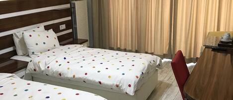 Habitación de hotel con dos camas, cabecero de madera, una mesa de comedor con una silla y un ventanal con cortinas.