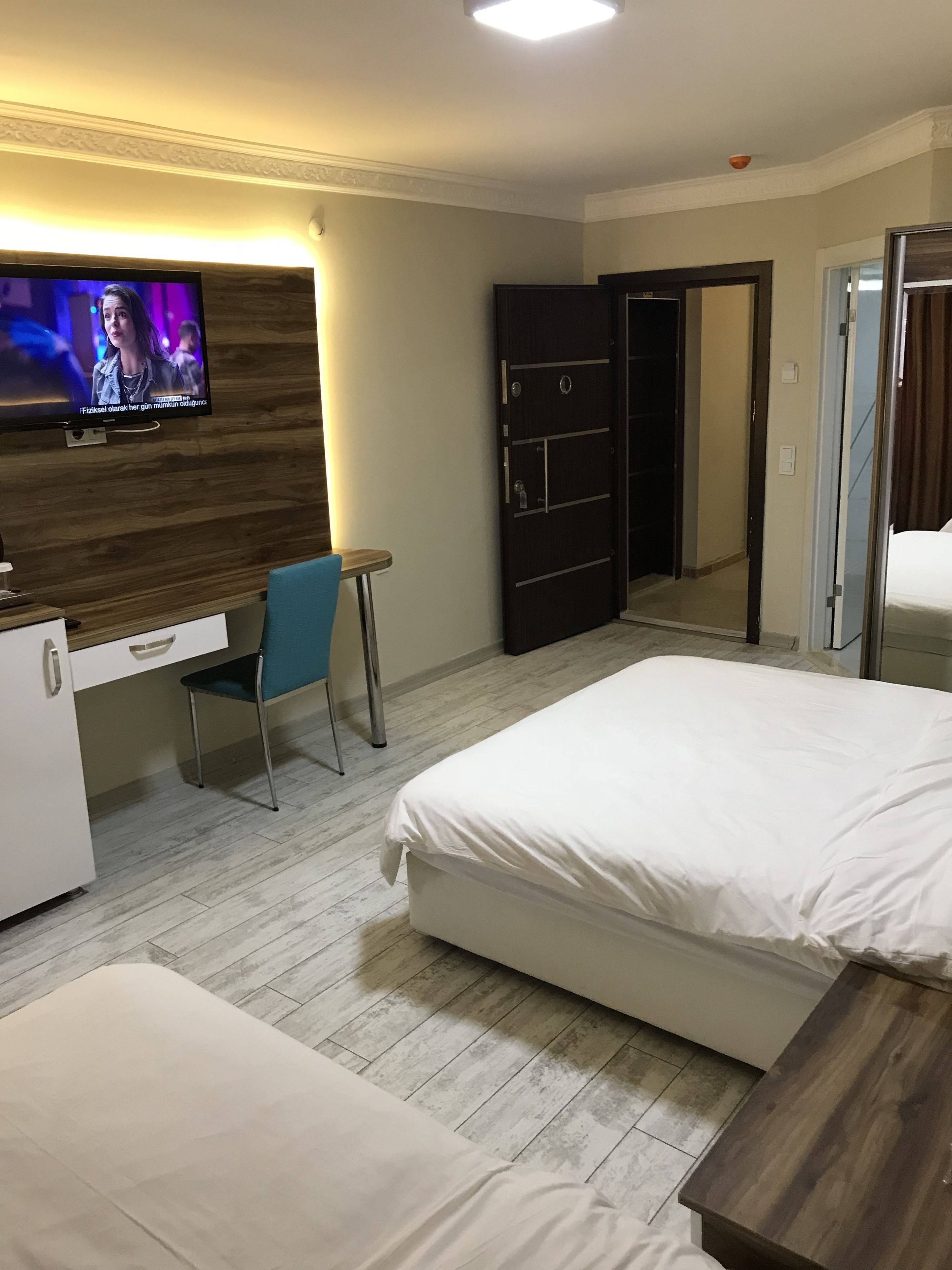 Une chambre d’hôtel avec deux lits, un bureau avec une chaise, un téléviseur fixé au mur et une armoire.