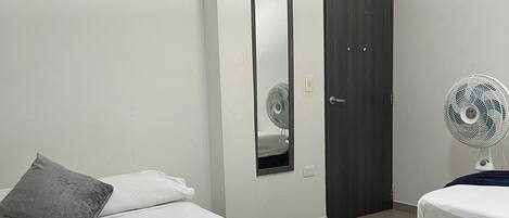 Une chambre moderne avec un grand lit, une table de chevet, un miroir, une armoire et un ventilateur sur pied.