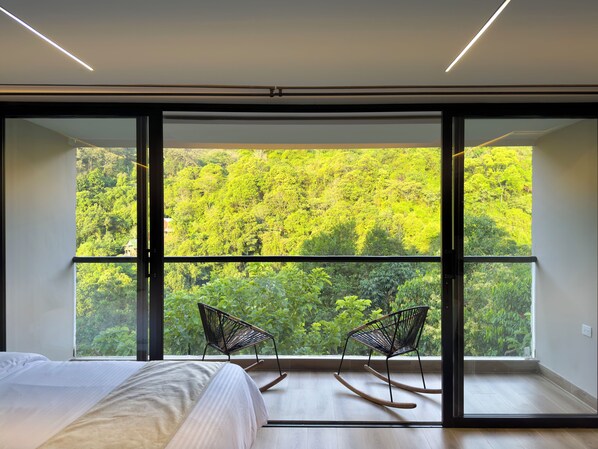 A bedroom with a large window, two rocking chairs, and a bed.