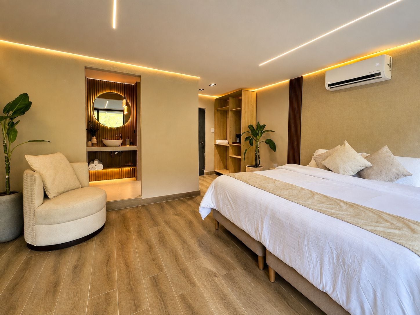 A modern hotel room with a bed, a seating area, a vanity with a mirror, and a built-in air conditioning unit.