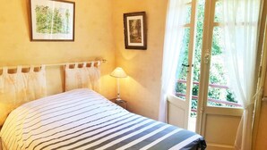 Une chambre avec une couvre-lit à rayures, deux tableaux encadrés au mur, une lampe de chevet et une fenêtre avec des rideaux.