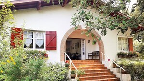 Une maison avec un escalier menant à une porte, entourée de verdure et bordée d’un mur rouge.