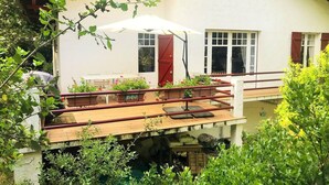 Une maison à deux étages avec un balcon, un coin repas avec du mobilier d’extérieur et une fenêtre avec une porte rouge.