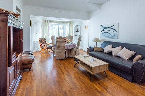A living room with a sofa, a coffee table, a dining area with chairs, and a wooden cabinet.