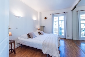 A bedroom with a double bed, bedside lamps, a small table, and a view of the outside through a window.