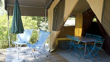 A tent with a table and chairs, a green umbrella, and a blue folding chair on a wooden deck.