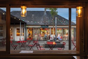 Un café al aire libre con mesas y sillas rojas, una terraza de madera y un edificio con un letrero que dice "Café Comptoir" al fondo.