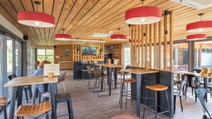 A modern restaurant interior with wooden ceiling, red pendant lights, and a bar area.