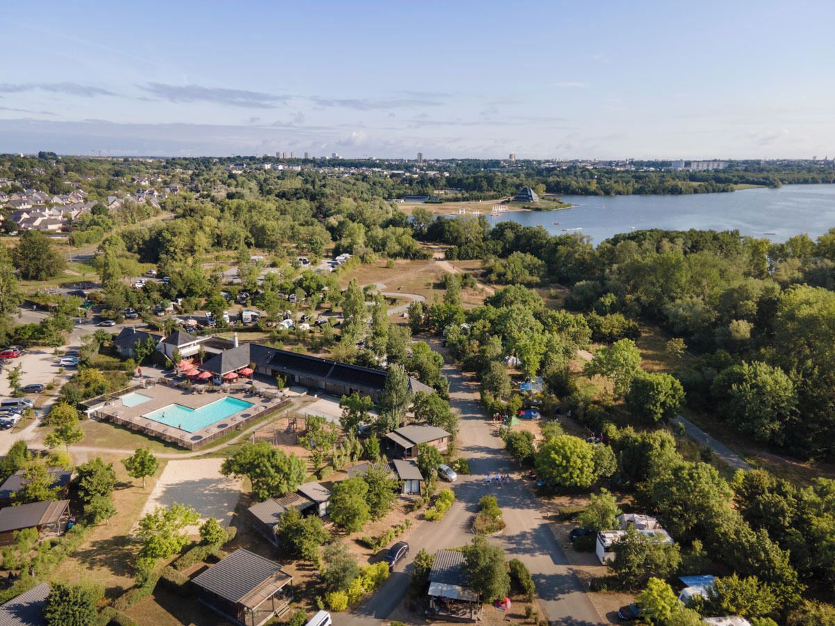 An aerial view of a resort with a swimming pool, multiple buildings, and a river in the background.