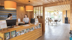 A wooden reception desk with two computers, a bulletin board, and a window with a view of the outdoors.