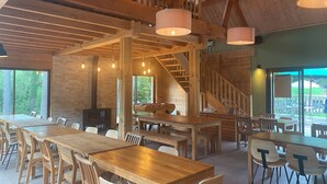 Un comedor amplio con mesas y sillas de madera, una escalera y ventanas grandes que ofrecen vistas del exterior.