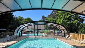 Una piscina con cerramiento de vidrio, rodeada de sillas de descanso y una terraza de madera.