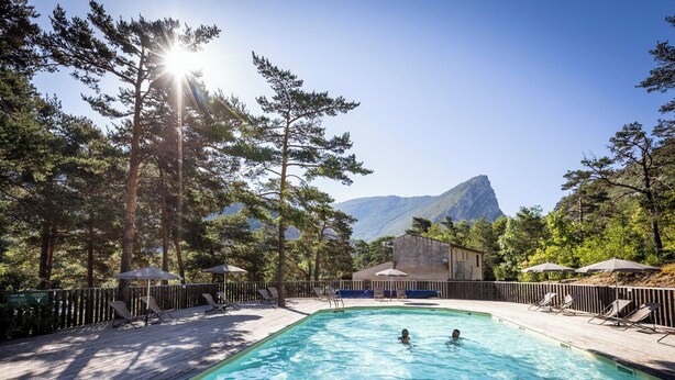 A swimming pool with lounge chairs and umbrellas, surrounded by trees and a mountain in the background.