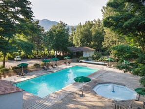 A rectangular swimming pool with a wooden deck, surrounded by lounge chairs and umbrellas. - Huttopia Millau (Millau)